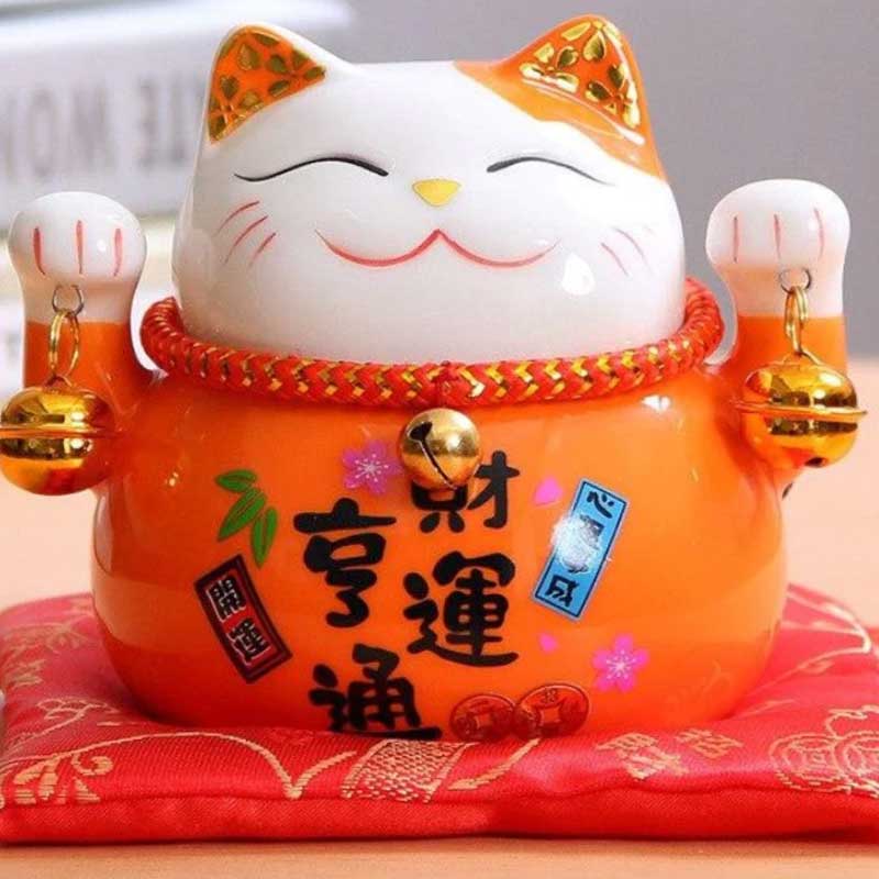 CE Chat Japon porte bonheur a les deux pattes levées et tient deux clochettes.