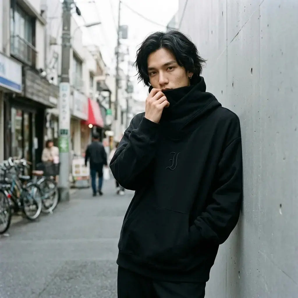 Hoodie streetwear noir de Tokyo porté avec le col cheminée remonté sur le bas du visage, contre un mur