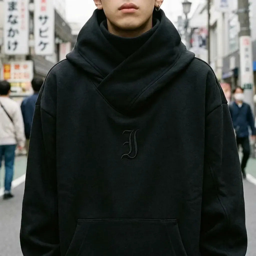 Vue rapprochée du col croisé du hoodie noir et du petit J gothique ton sur ton sur la poitrine