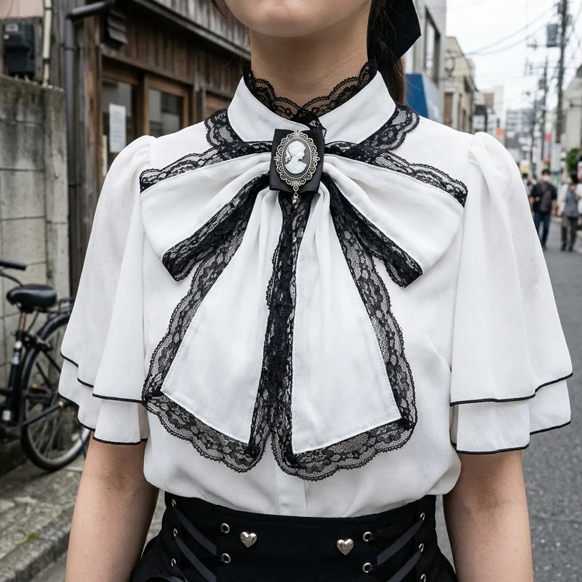 Vue rapprochee du noeud noir borde de dentelle, de sa broche camee argentee et du col cape de la blouse