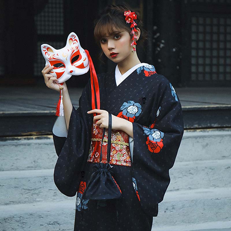 Une femme est habillée avec un obi ceinture de kimono japonais. Elle tient dans la main un masque Kitsune de renard japonais