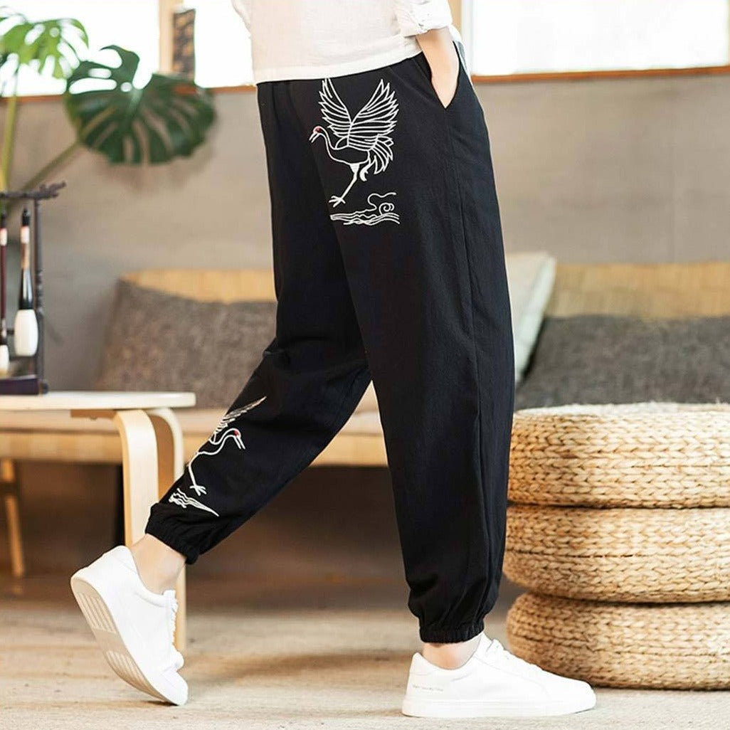 Homme portant un pantalon japonais noir orné de grues blanches, associé à une chemise blanche et des baskets blanches