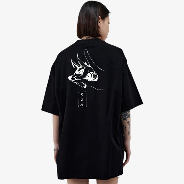 Une femme japonaise de dos est habillée avec le T-shirt Kon. C'est un t-shirt manga de couleur noire et en matière coton. Le t-shirt manga est inspiré du manga chainsaw man. La forme de doigts dans le dos permet a Aki d'appeler le demon Kitsune