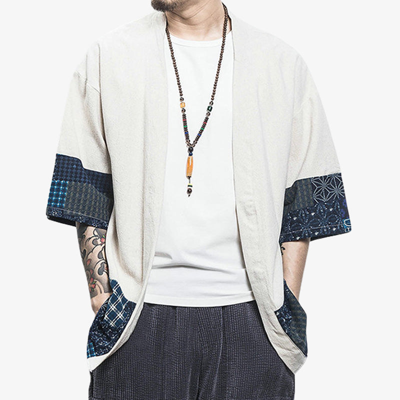 Un homme se tient debout et est habillé avec un vetement japonais cardigan court. Cet habit est une veste de kimono qui s'enfile par-dessus un t-shirt pour un style vestimentaire zen japonais et décontracté. La veste haori est de couleur blanche. Il a un chaplet du bouddhisme zen autour du cou