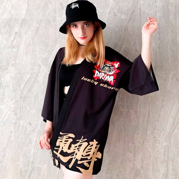 Une vemme porte une veste de kimono noir avec des écritures Kanji et un motif daruma imprimé