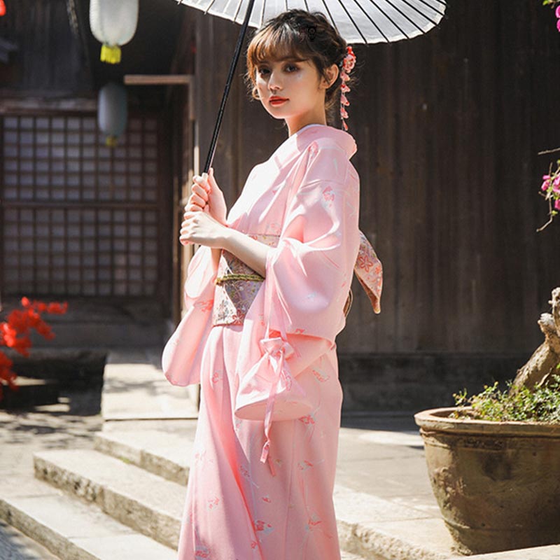 Une femme est vêtue d'un kimono japonais traditionnel et d'un ceinture de geisha Obi autour de la taille. Elle tient dans la main une ombrelle japonaise. La geisha a un Kanzashi dans les cheveux