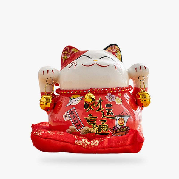Un chat japonais porte bonheur de couleur rouge et en céramique. Le chat de la chance a lles deux pates levées et tient des clochettes. Il est est peint avec des Kanji