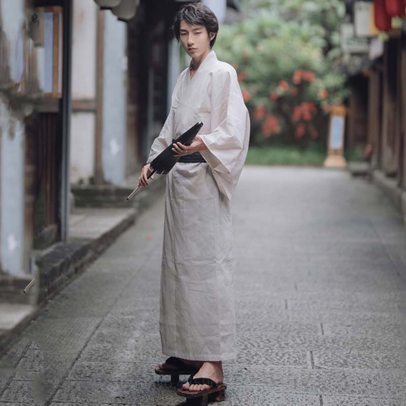 Un homme est habillé avec un kimono japonais blanc, et des sandales japonaises Geta. Le yukata est attaché a la taille avec une ceinture japonaise obi