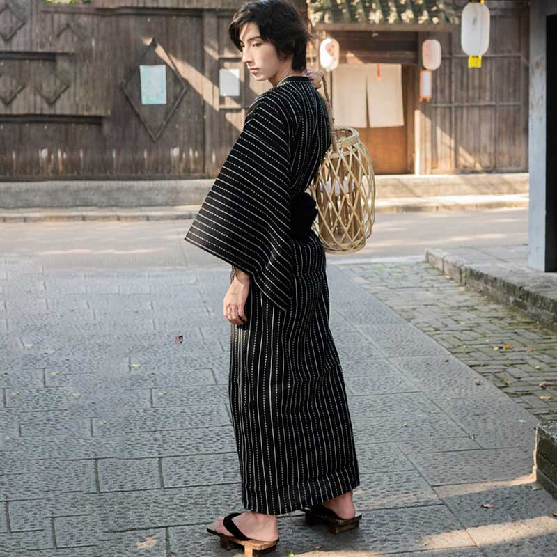 Un adolescent de dos est vêtu d'un kimono japonais homme noir. Il a au pied des sandales japonaises Geta
