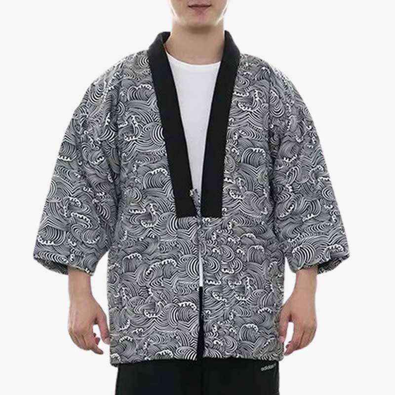 Un homme se tient debout et est habillé avec une veste Hanten Nami. Le col du manteau japonais est noir et le tissu est parsemé de motifs de vagues japonaises blanches