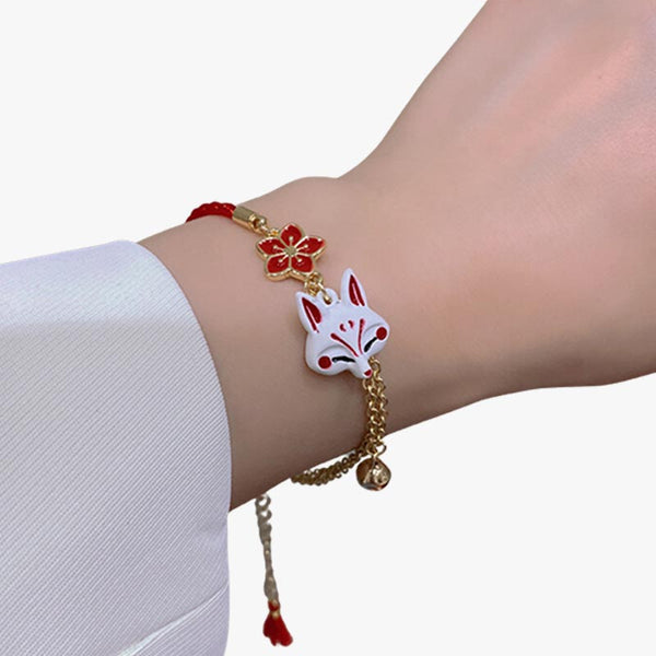 Une femme porte au poignet un bracelet japonais Kitsune avec une chaine en or, une tête de renard Kitsune et un symbole de fleur de sakura