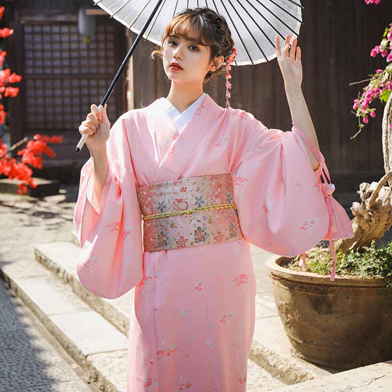 Une femme est habillée avec un kimono japonais attaché avec une ceinture geisha avec des motifs floraux brodés sur le tissu. La femme japonaise tient dans sa main une ombrelle