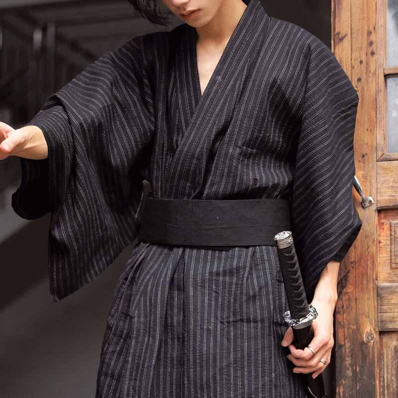 Un homme est habillé avec un kimono noir et un ceinture japonaise samourai. Il tient dans la main un épée Katana