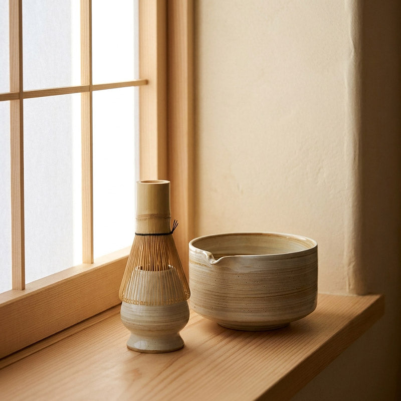 Bol à matcha et support en céramique sur un plan de bois éclairé par une lumière naturelle douce