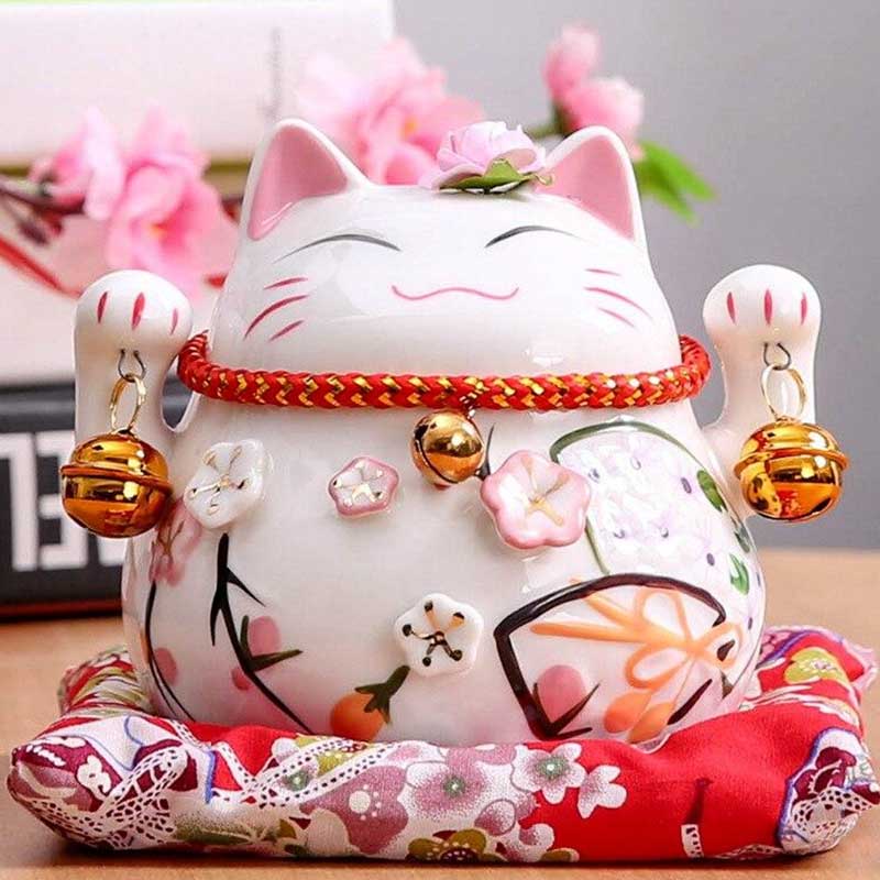 le chat maneki neko porte bonheur est un objet décoration japonaise posé sur un coussin rouge et une étagere
