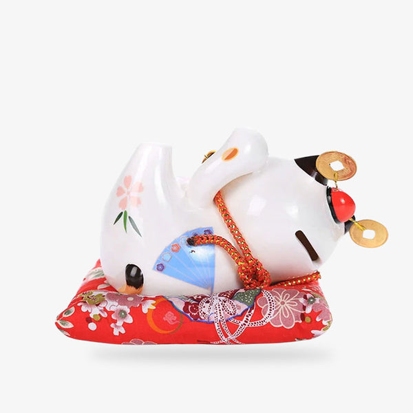un chat japonais ceramique allongé sur un coussin rouge