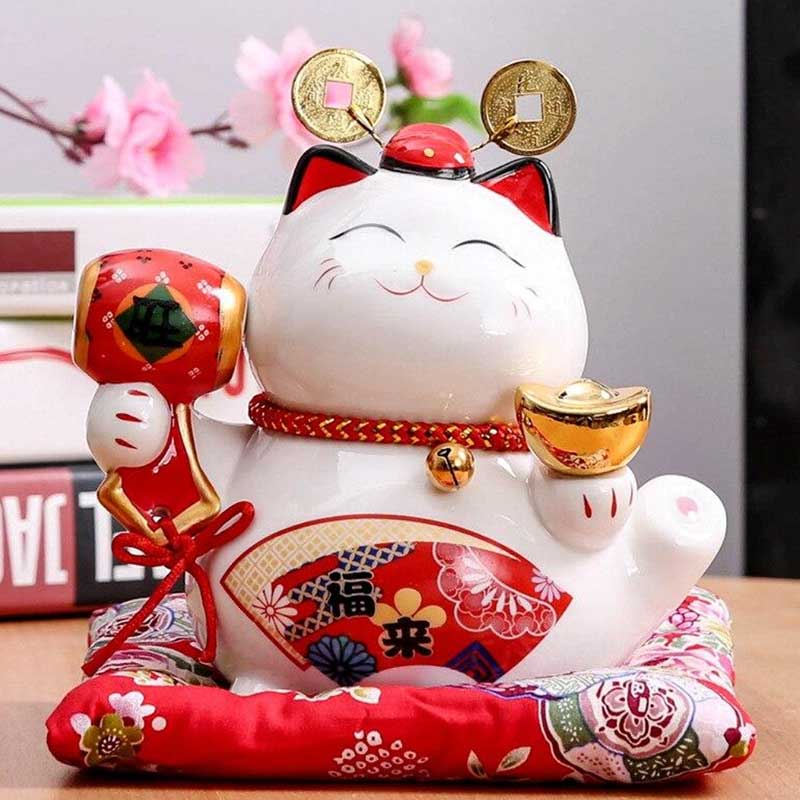 Le chat japonais lucku maneki neko est de couleur blanche. Il a kla patte droite levée et tient un maillet de couleur rouge avec un kanji. Des dessins d'eventails sensu sont peints à la main. La petite statuette est posée sur un coussin rouge