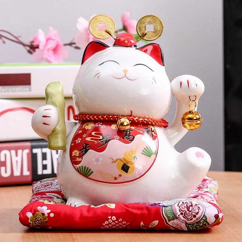 Un chat japonais maneki neko achat est sur une étagère en boir. Il tient une clochette dans sa patte gauche levée