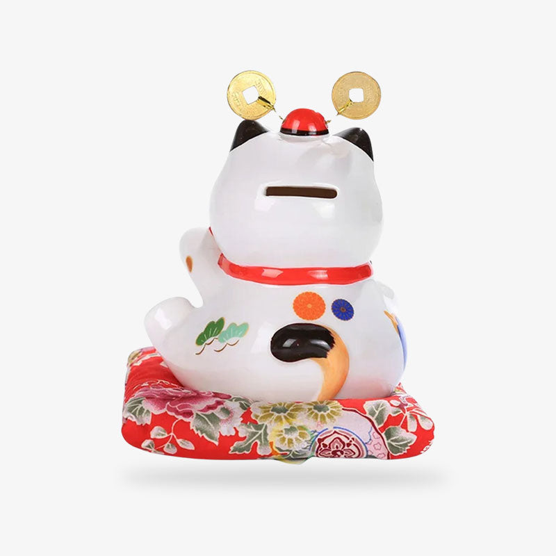 Ce chat japonais porte bonheur a une fente au niveau de la tete. C'est une tirelire maneki neko posée sur un coussin rouge