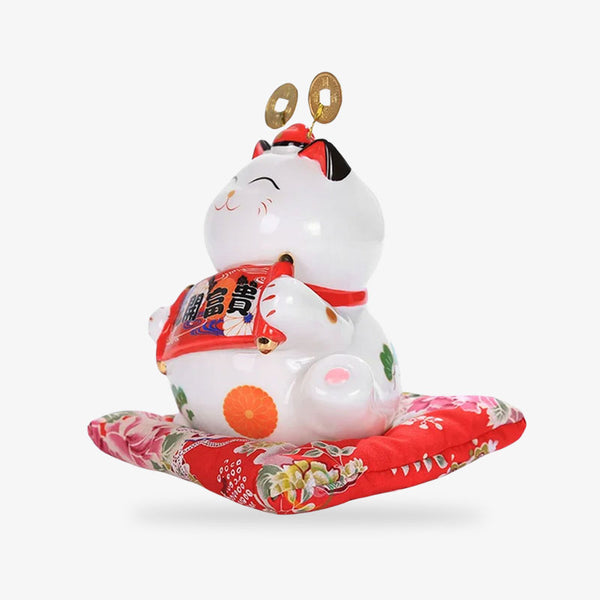 Ce chat porte-bonheur du Japon est un chat maneki neko fabriqué en céramique et de couleur blanche. C'est un objet deco japonaise posé sur un coussin rouge