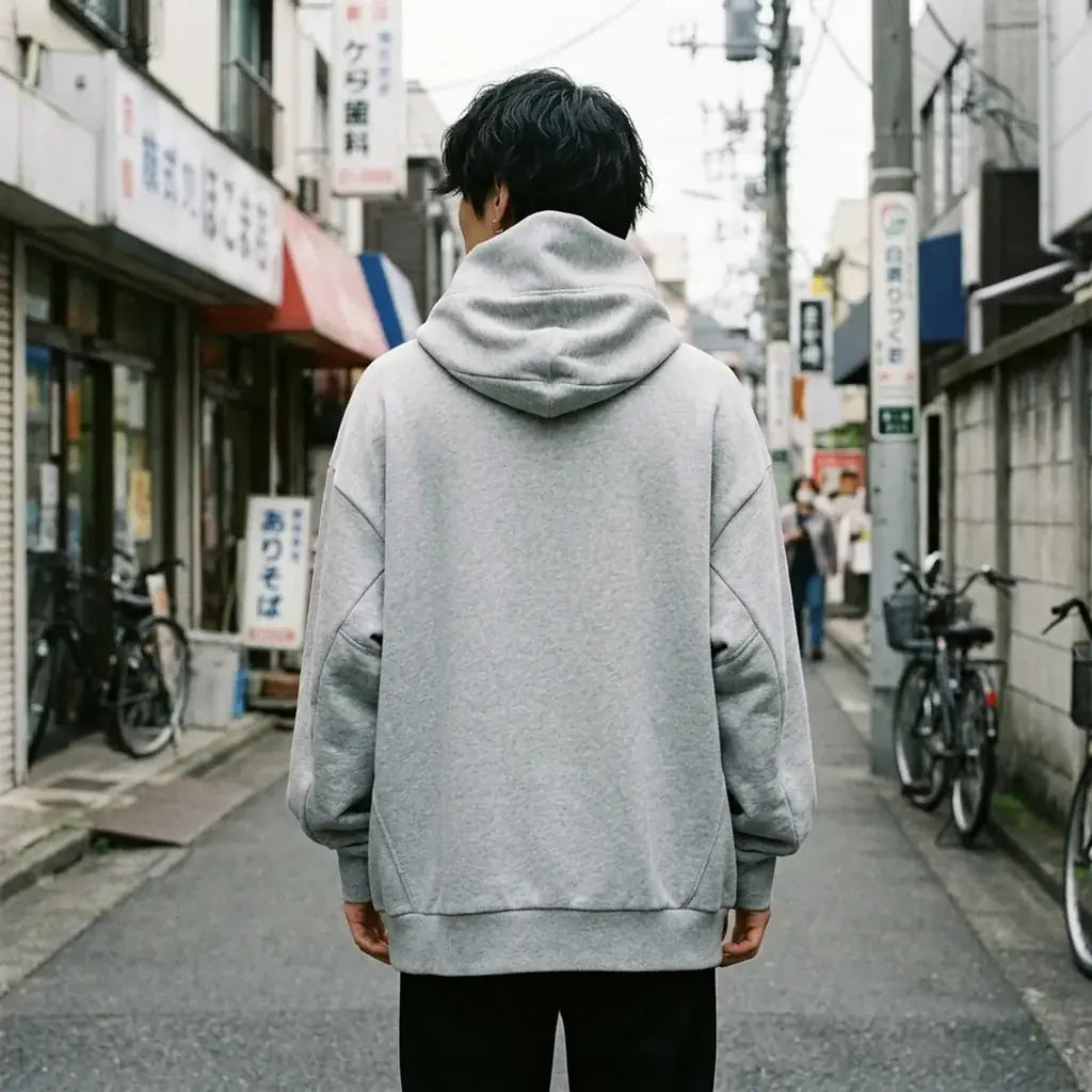Dos du sweat à capuche gris oversize, uni gris chiné, avec la haute capuche cheminée qui se dresse derrière la tête.