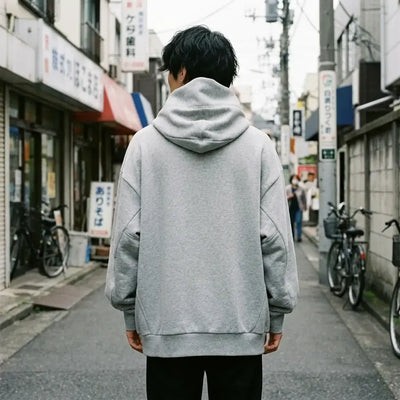 Dos du sweat à capuche gris oversize, uni gris chiné, avec la haute capuche cheminée qui se dresse derrière la tête.