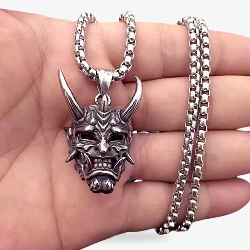 Un homme tient dans la main un collier yokai avec un pendentif japonais de démon oni avec des cornes et des crocs