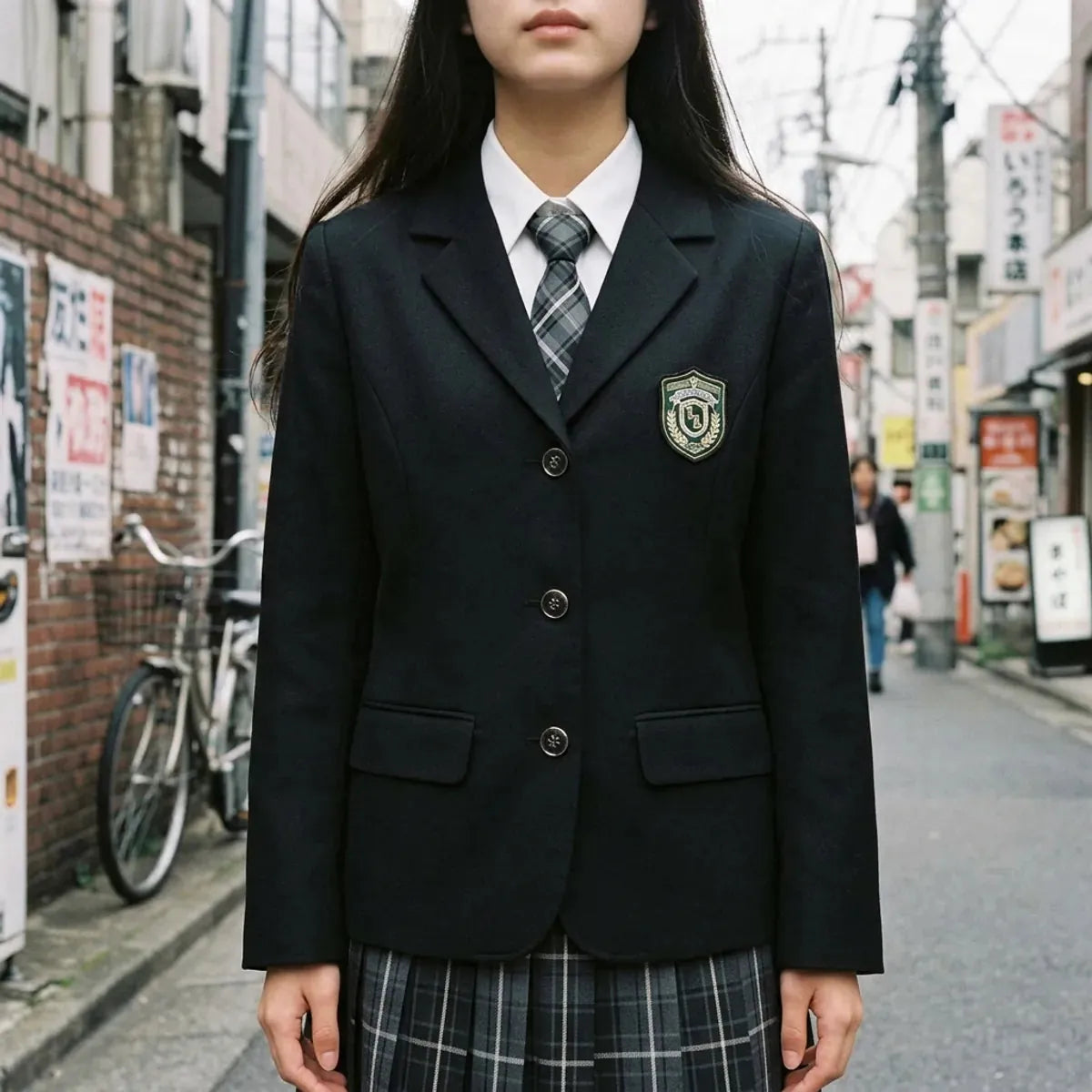 Vue rapprochée du blazer scolaire noir, de l'écusson brodé en forme de bouclier, du col blanc et de la cravate à carreaux