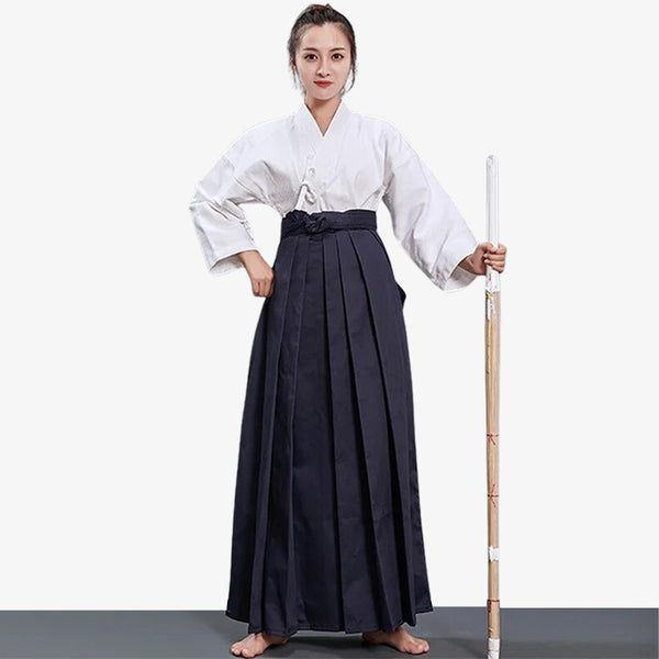Une pratiquante d'arts martiaux japonais est vêtue d'un hakama femme, d'un keikogi blanc et tient dans la main un sabre katana en bois shinai