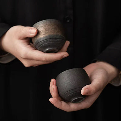 Un homme en vêtement noir tient deux tasses à matcha en céramique au savoir-faire raffiné, idéales pour sublimer l'expérience du thé japonais