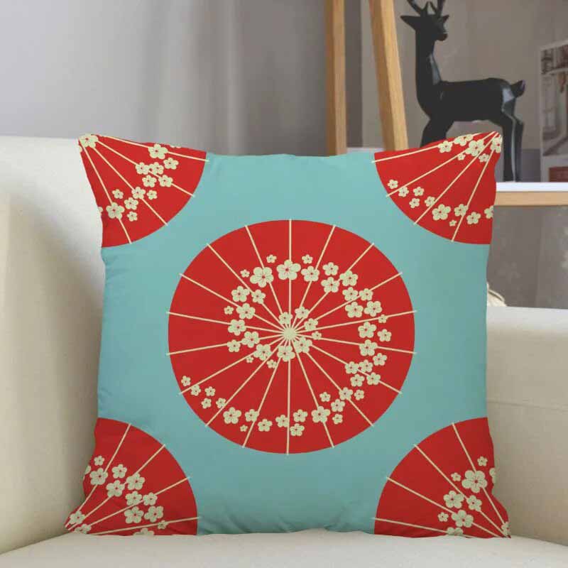 Une housse de coussin au design japonais de couleur rose est posé sur un canapé. Des ombrelles japonaises de couleur rouge des motifs sakura sont imprimés sur le tissu de la housse