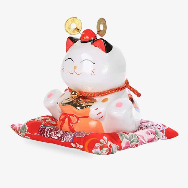 Le Japon Chat porte bonheur est une tirelire en céramique sur un coussin rouge
