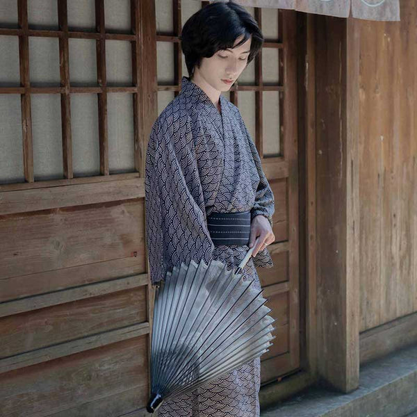 Un japonais est habillé avec un kimono coton homme. Le motif seigaiha est imprimé sur le tissu du Yukata. L'habit traditionnel est fermé avec une ceinture Obi. L'homme tient dans la main une ombrelle japonaise