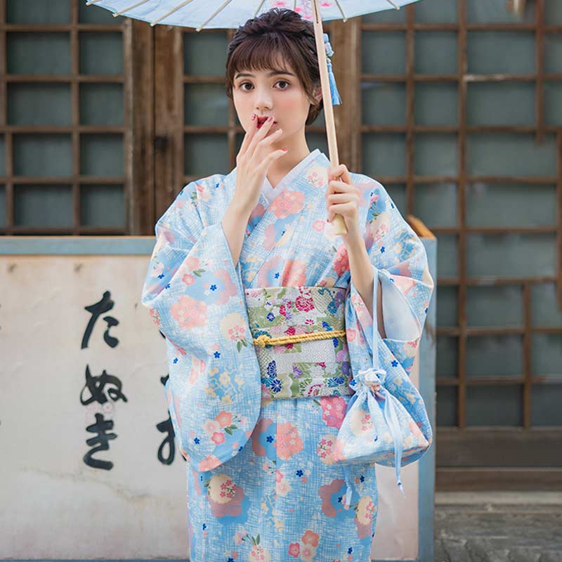 Une femme porte une robe kimono Hanabatake, tissu bleu à motif floral japonais, tenant un sac kimono assorti