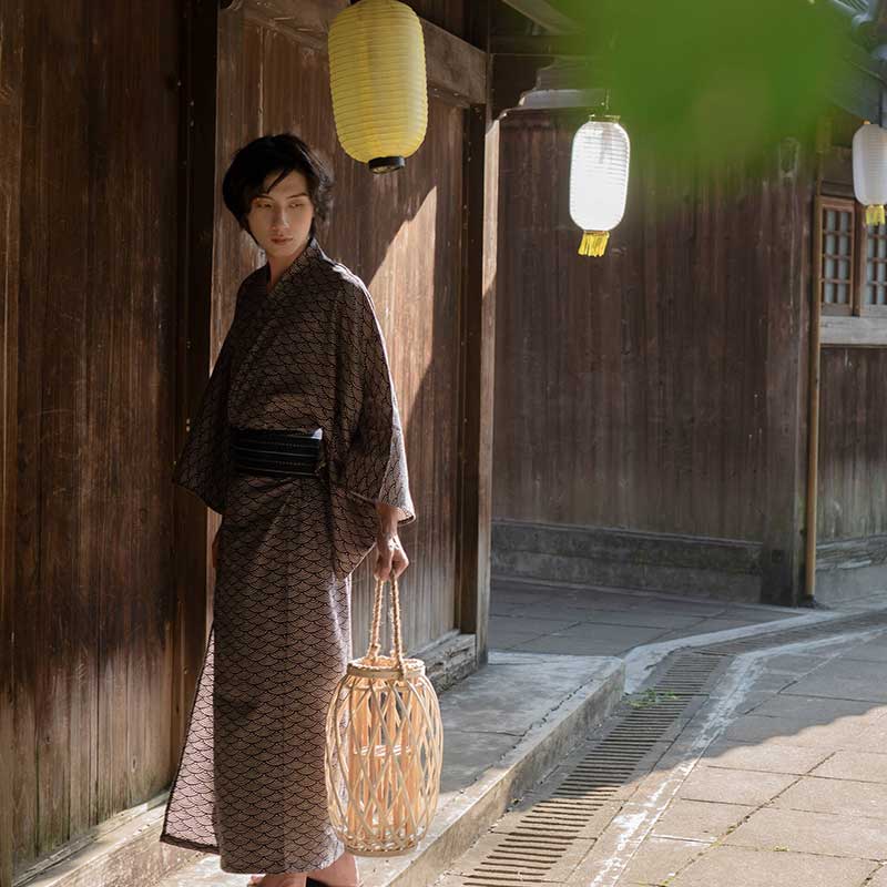 Un japonais est debout dans une rue a Kyoto. Il est habillé avec un kimono Yukata et une ceinture japonaise Obi. Il tient dans la main une lanterne japonaise