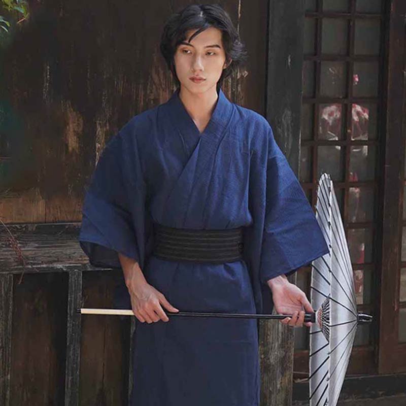 Un individu est habillé avec un kimono japonais homme samurai. Son kimono traditionnel est attaché avec une ceinture Obi. Il tient une ombrelle japonaise dans la main