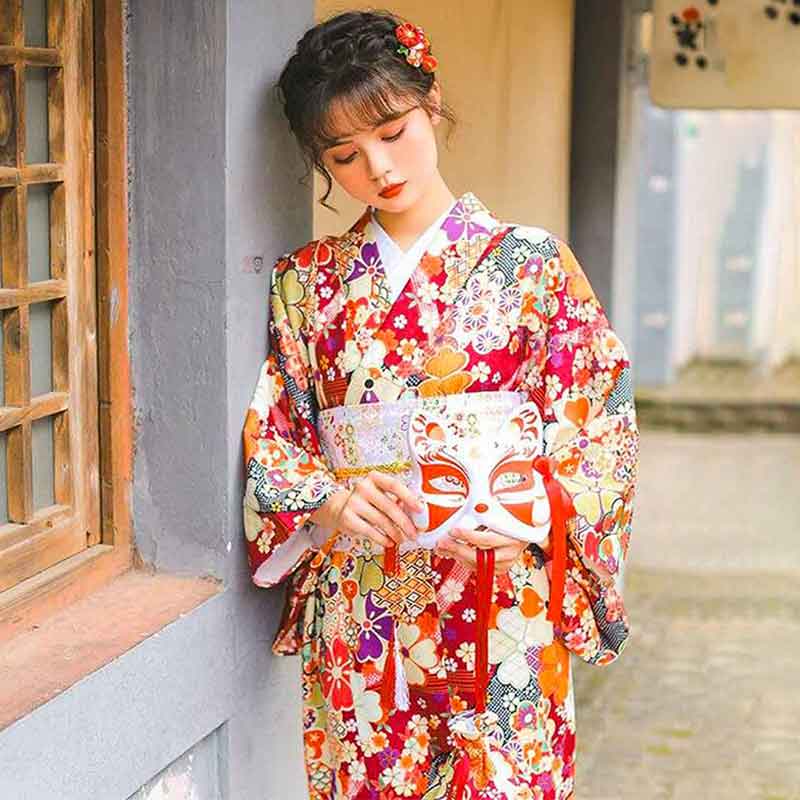 Kimono rouge japonais orné de motifs de fleurs de sakura, la femme tient un masque kitsune dans sa main
