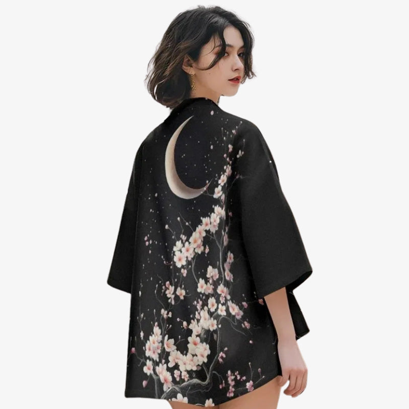 Une femme porte un kimono Sakura orné de délicats motifs de fleurs de cerisier et de lune, évoquant la beauté du printemps japonais