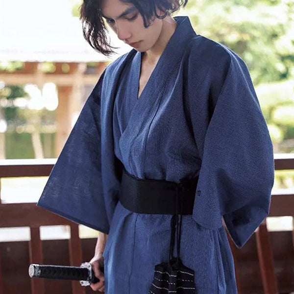 Un hoimme porte un kimono yukata japonais de couleur bleu. Le kimono japonais est attaché avec une ceinture Obi noir