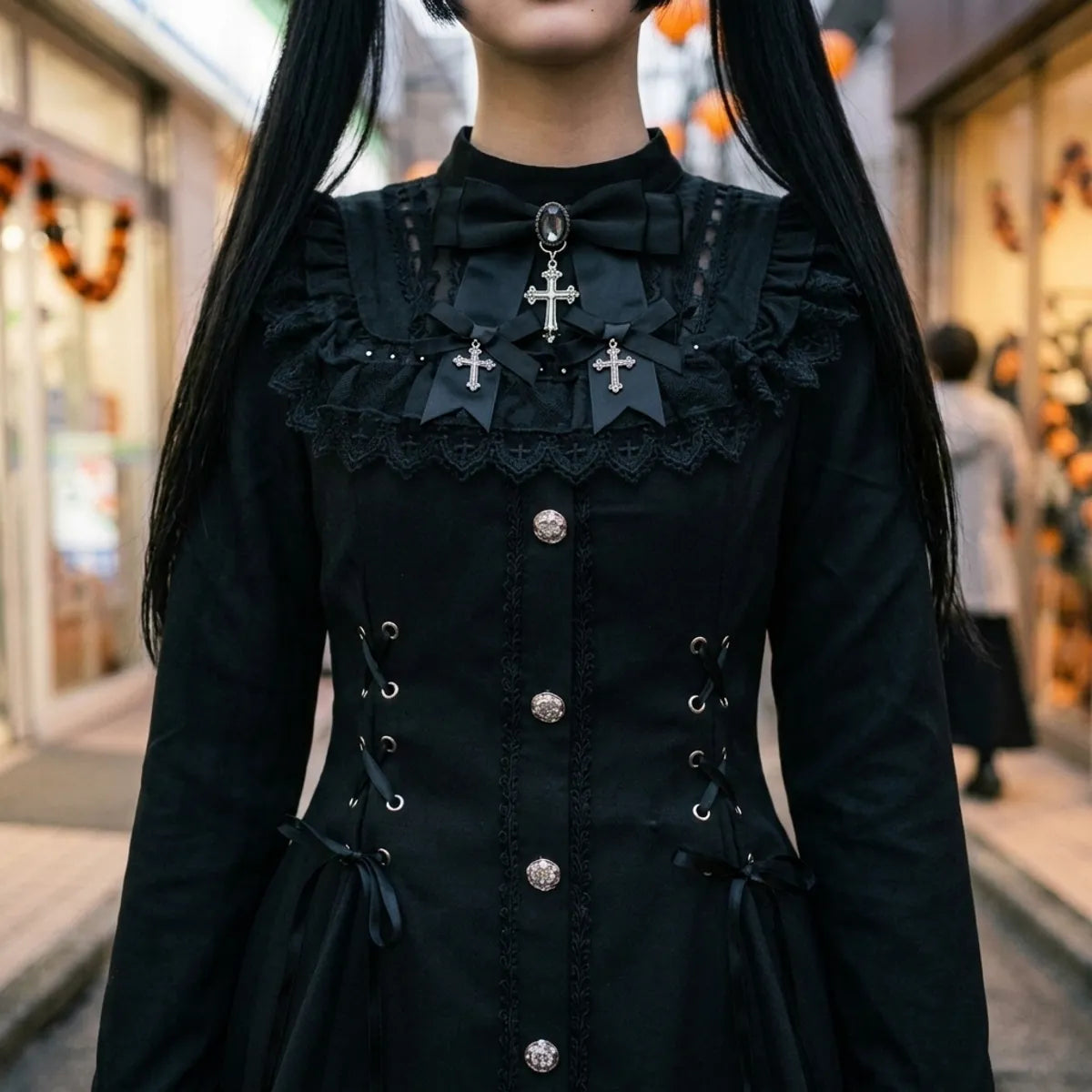 Vue rapprochée du laçage du corset, des boutons argentés et du col en dentelle noire orné de motifs en croix.