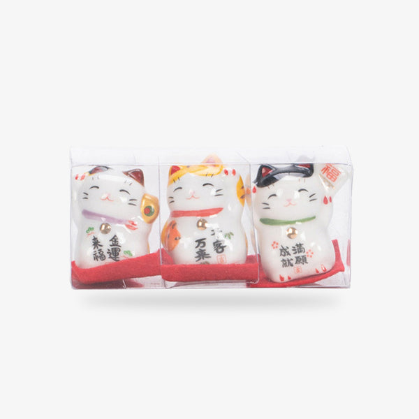 trois figurines de maneki neko blanc peints à la main avec une écriture japonaise Kanji. Les chats porte-bonheur levent leur pates gauches. Ils sont emballés dans une boite transparente