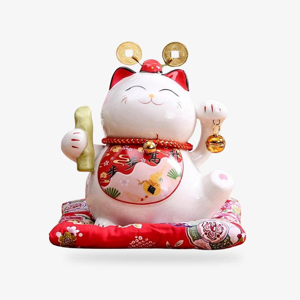 Ce maneki neko chat japonais est de couleur blanche. Sa patte droite est levée pour attirer la chance, la bonne fortune et la prospérité. Cette statuette est un chat porte-bonheur fabriqué en céramique. Le chat japonais est posé sur un coussin rouge