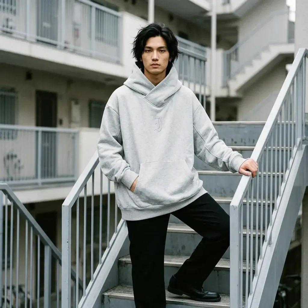 Sweat à capuche gris chiné pour homme, porté debout sur les marches en béton d'un immeuble à Tokyo.