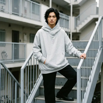 Sweat à capuche gris chiné pour homme, porté debout sur les marches en béton d'un immeuble à Tokyo.
