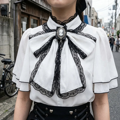 Vue rapprochee du noeud noir borde de dentelle, de sa broche camee argentee et du col cape de la blouse