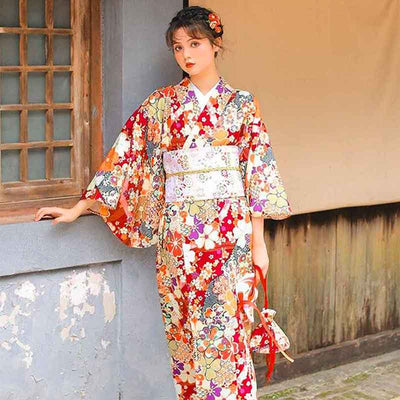 Femme portant un kimono japonais rouge à motifs de sakura, ceinturé d'un large obi japonais