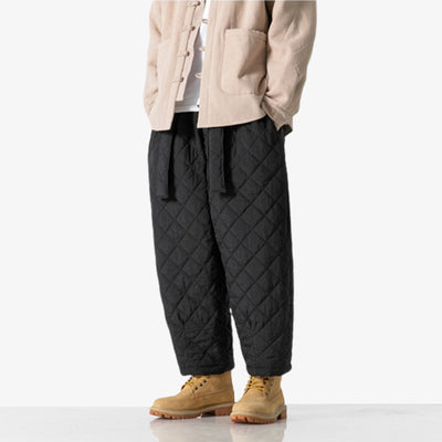 Un homme se tient debout avec un pantalon cargo style japonais noir, une veste beige et des timberland chaussures de montagne
