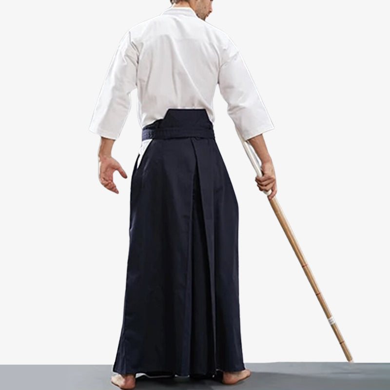 Un pratiquant de Kendo est équipé d'un pantalon hakama homme. Il tient dans la main un shinai. Ils est habillé avec un keikogi blanc