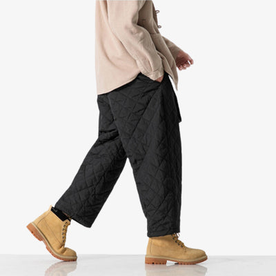 Un homme marche avec un pantalon japonais ample de couleur noire et à la matière imperméable