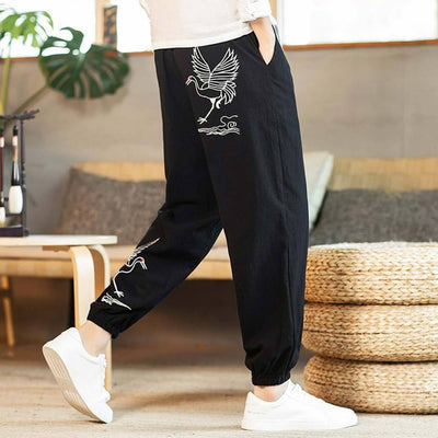 Homme portant un pantalon japonais noir orné de grues blanches, associé à une chemise blanche et des baskets blanches